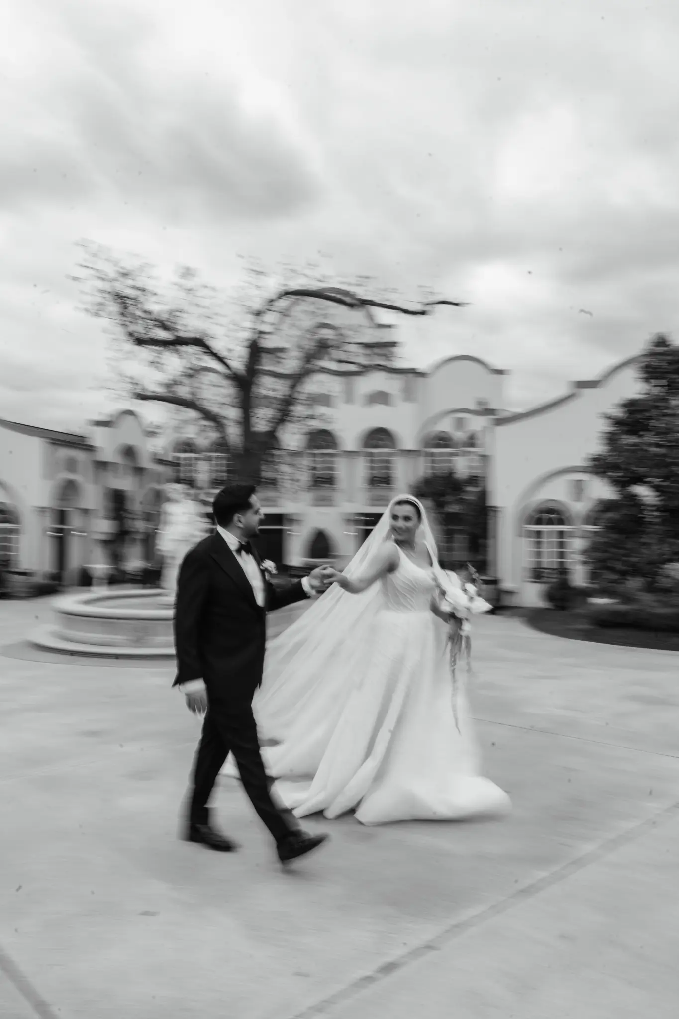 Black and white motion-blur portrait of a bride and groom walking outside an ornate building