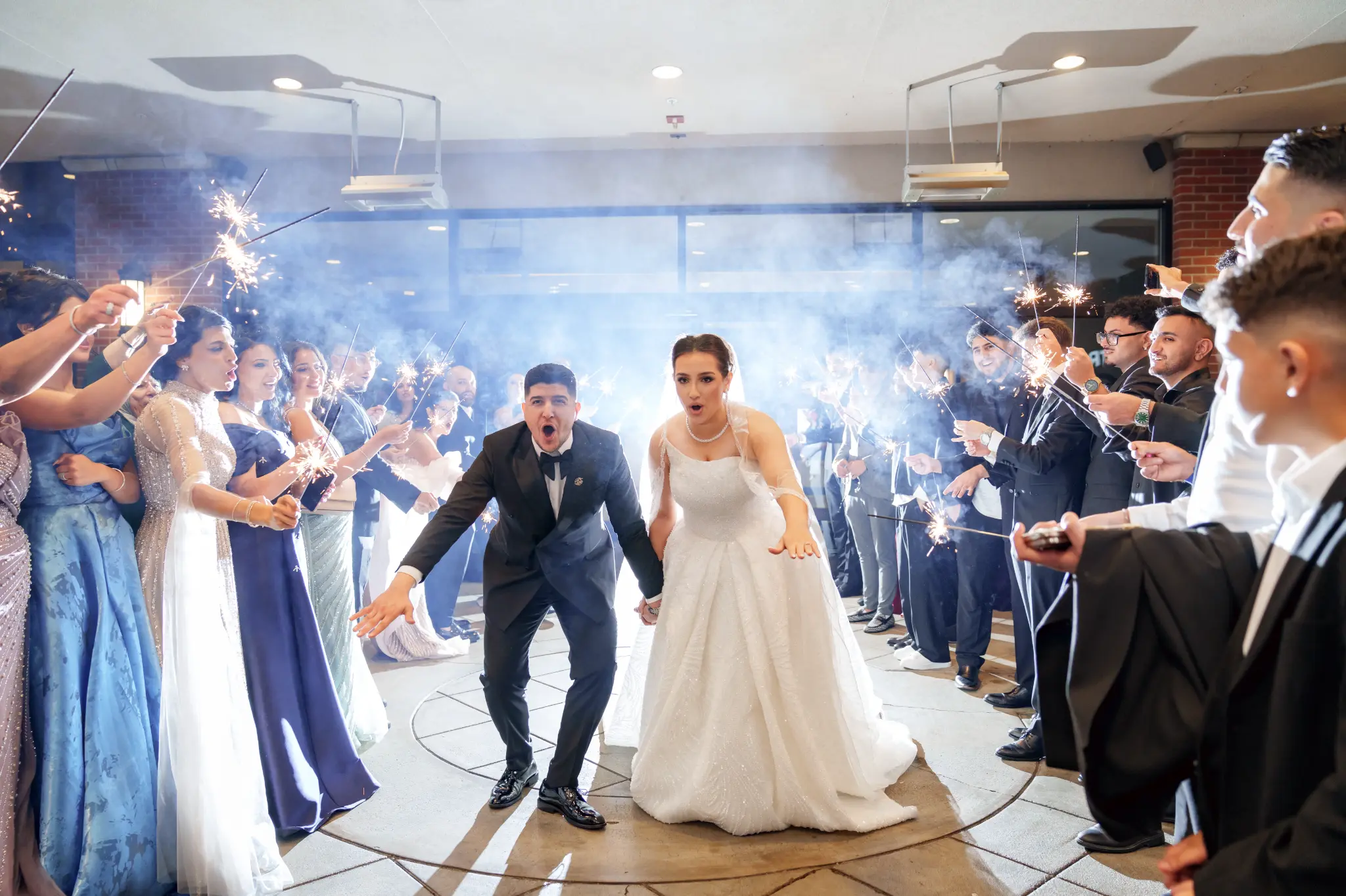 Bride and groom walking through guests holding lit sparklers amid smoke
